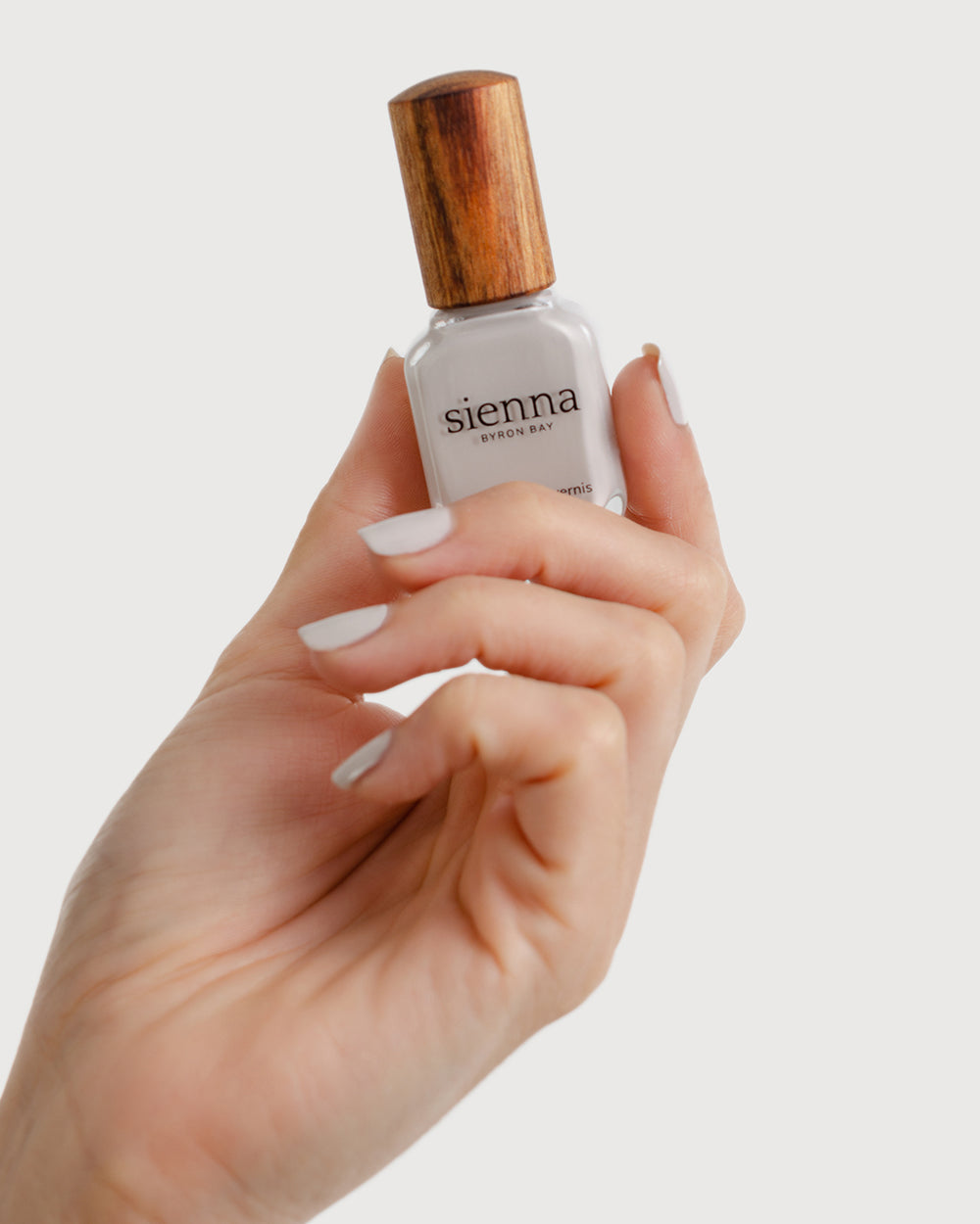 Light cool-grey nail polish hand swatch on fair skin tone holding sienna bottle