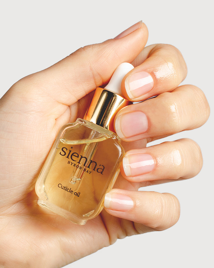 fair skin tone hand holding bottle of cuticle oil 