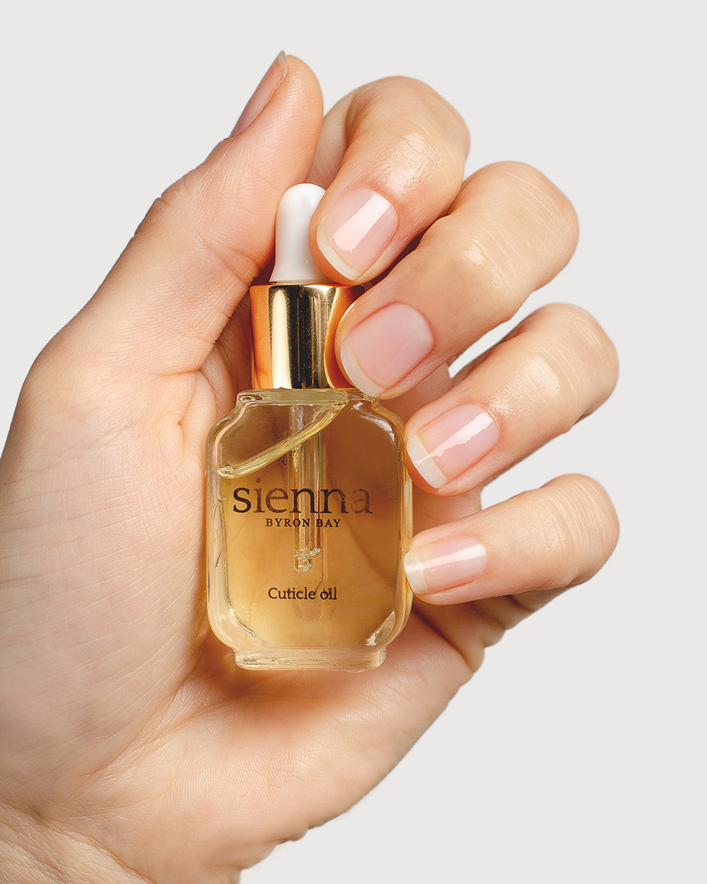 fair skin tone hand holding bottle of cuticle oil close up