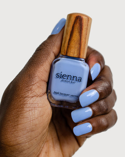 periwinkle blue nail polish hand swatch on dark skin tone holding a sienna bottle