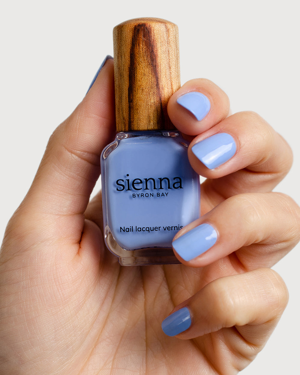 periwinkle blue nail polish hand swatch on fair skin tone holding a sienna bottle 