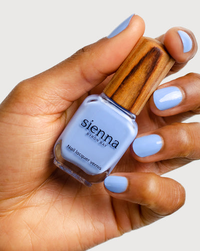periwinkle blue nail polish hand swatch on medium skin tone holding a sienna bottle