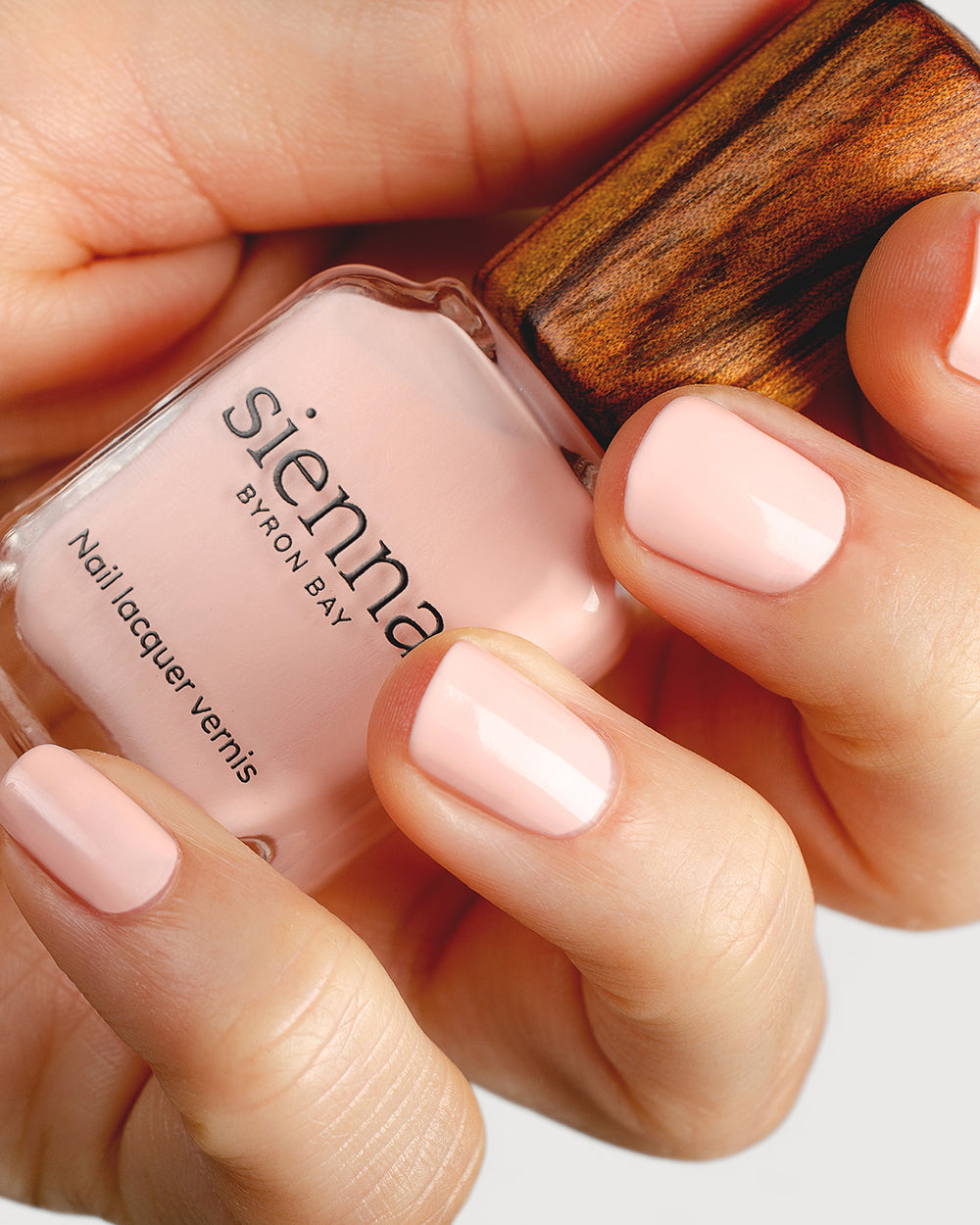 pastel pink nail polish hand swatch on fair skin tone holding a sienna bottle up close