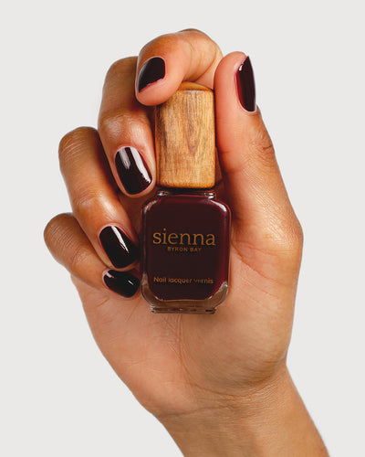 dark red nail polish hand swatch on medium skin tone holding a sienna bottle