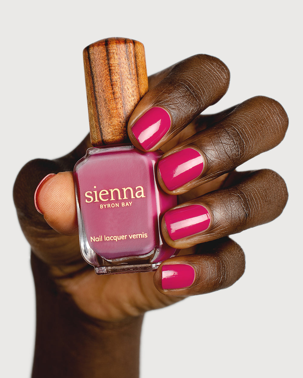 fuschia pink nail polish hand swatch on dark skin tone  holding a sienna bottle