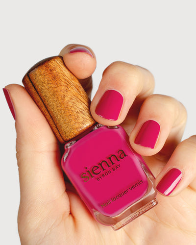 fuschia pink nail polish hand swatch on fair skin tone holding a sienna bottle