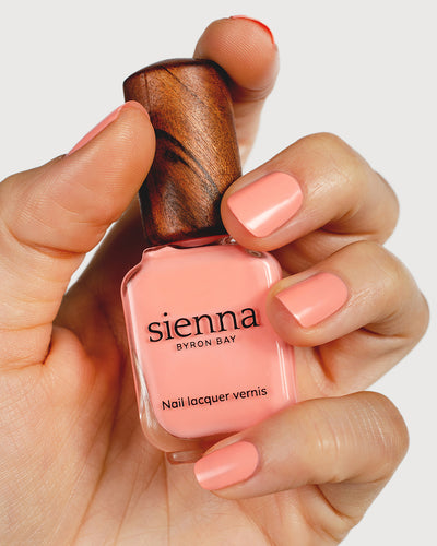 Vibrant peach nail polish hand swatch on fair skin tone holding sienna bottle up close