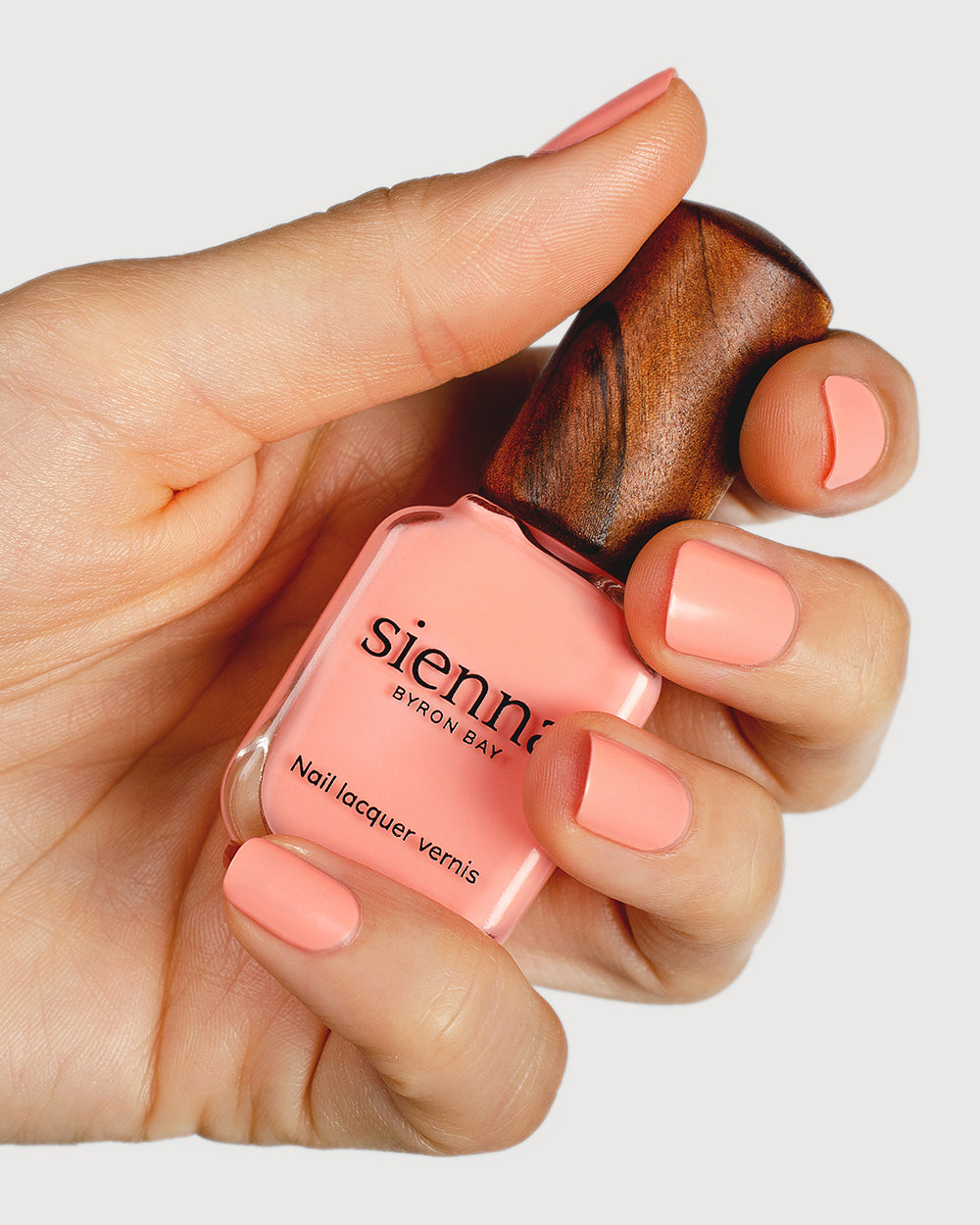 Vibrant peach nail polish hand swatch on fair skin tone holding sienna bottle