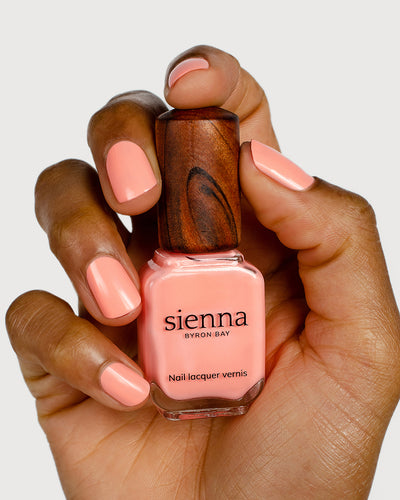 Vibrant peach nail polish hand swatch on medium skin tone holding sienna bottle