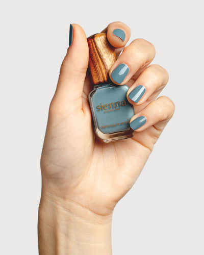 mid grey-blue nail polish hand swatch on fair skin tone holding sienna bottle