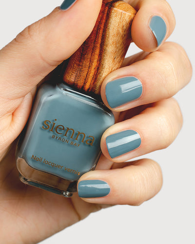 Mid grey-blue nail polish hand swatch on fair skin tone holding sienna bottle close-up