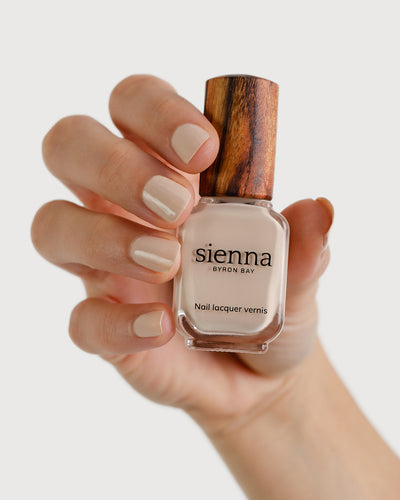 Classic beige nail polish hand swatch on fair skin tone holding sienna bottle