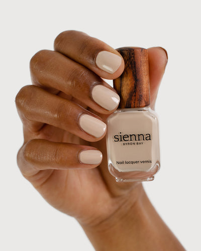 Classic beige nail polish hand swatch on medium skin tone holding sienna bottle