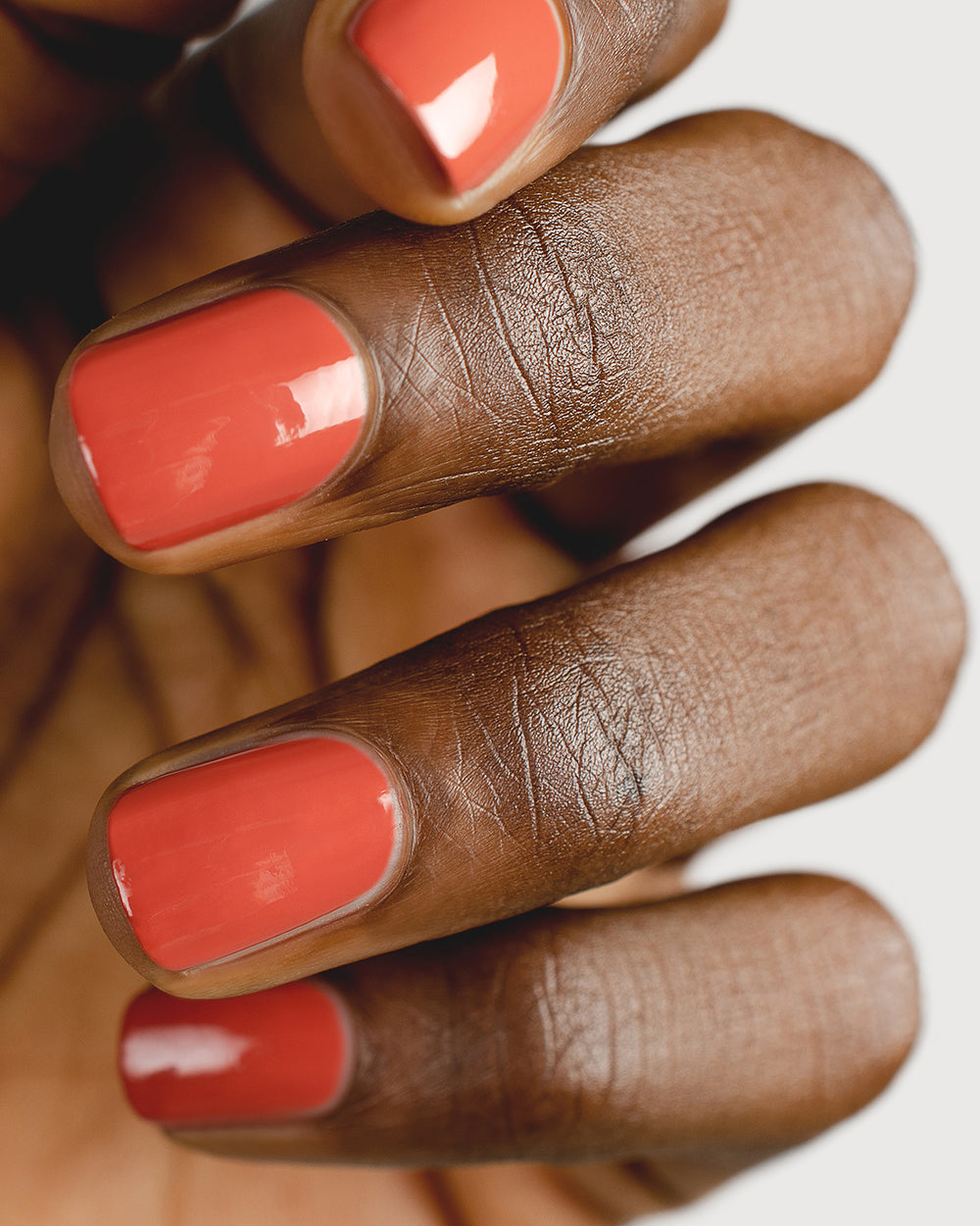 Brick red nail polish hand swatch on dark skin tone up-close