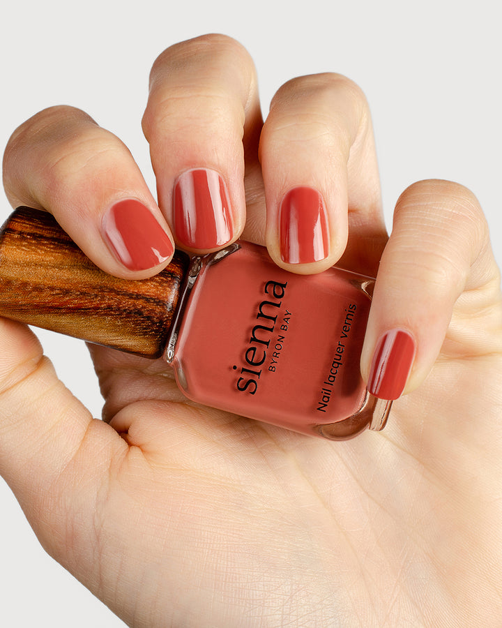 brick red nail polish hand swatch on fair skin tone holding sienna bottle