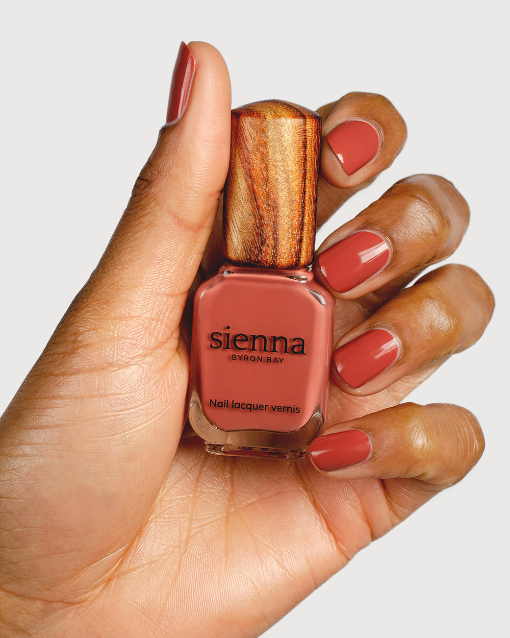 brick red nail polish hand swatch on fair skin tone holding sienna bottle