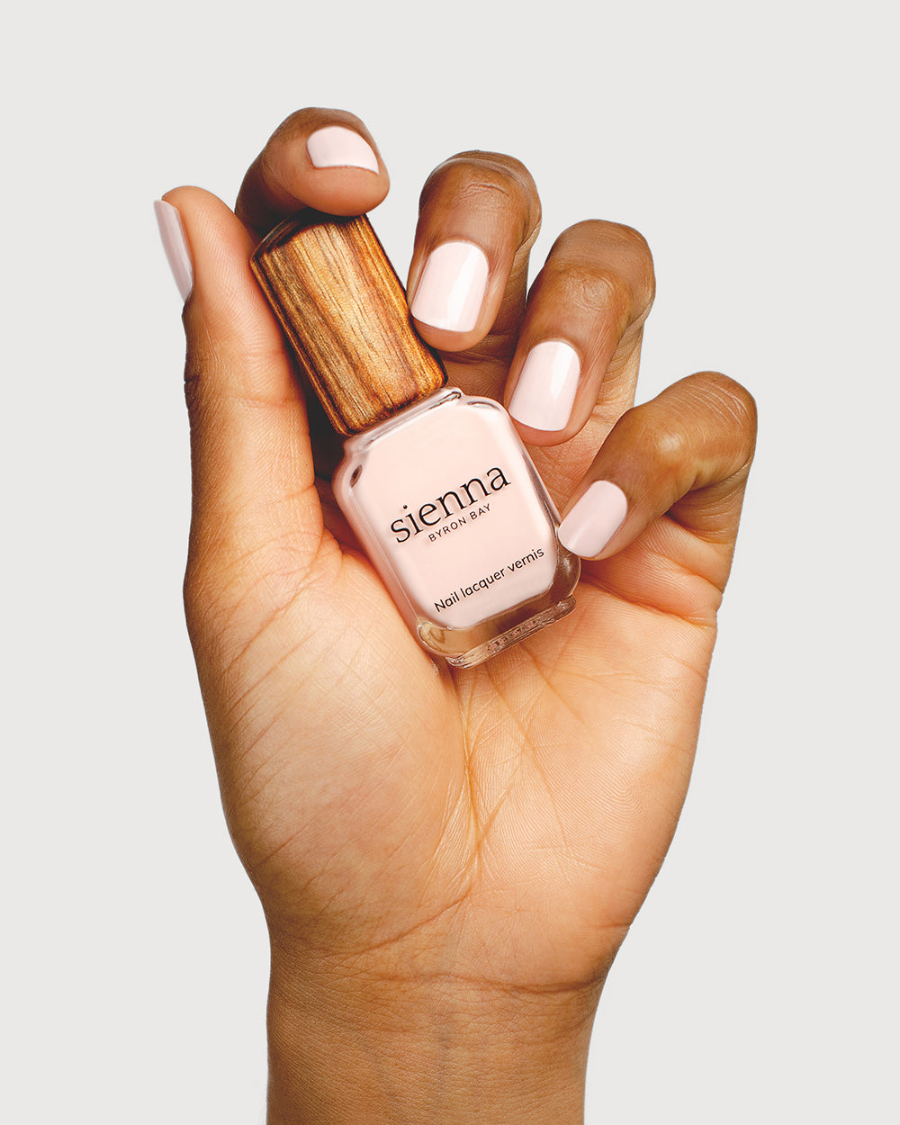 rosewater pink nail polish hand swatch on medium skin tone holding sienna bottle