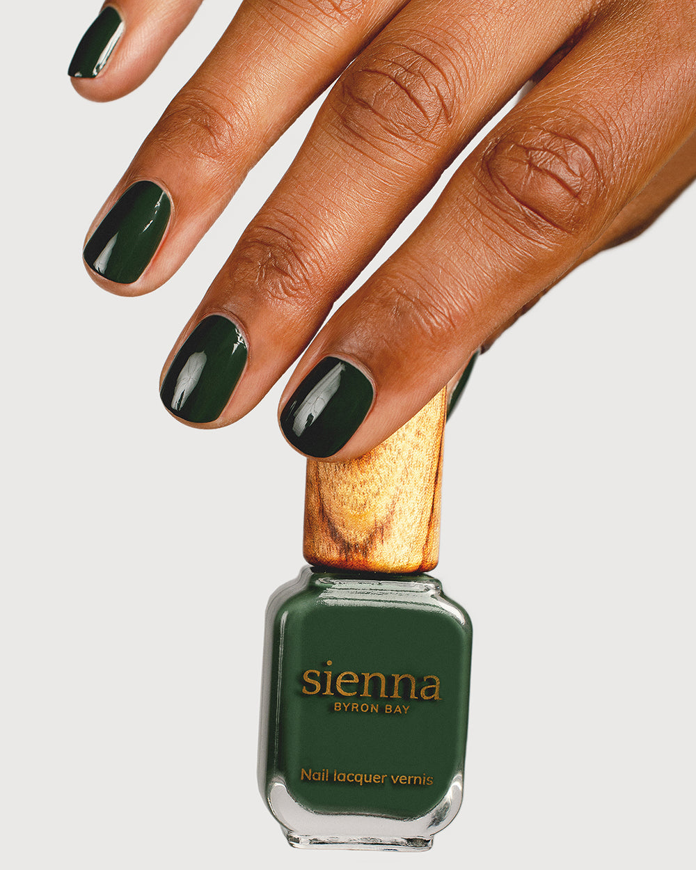 deep olive green nail polish hand swatch on medium skin tone holding sienna bottle
