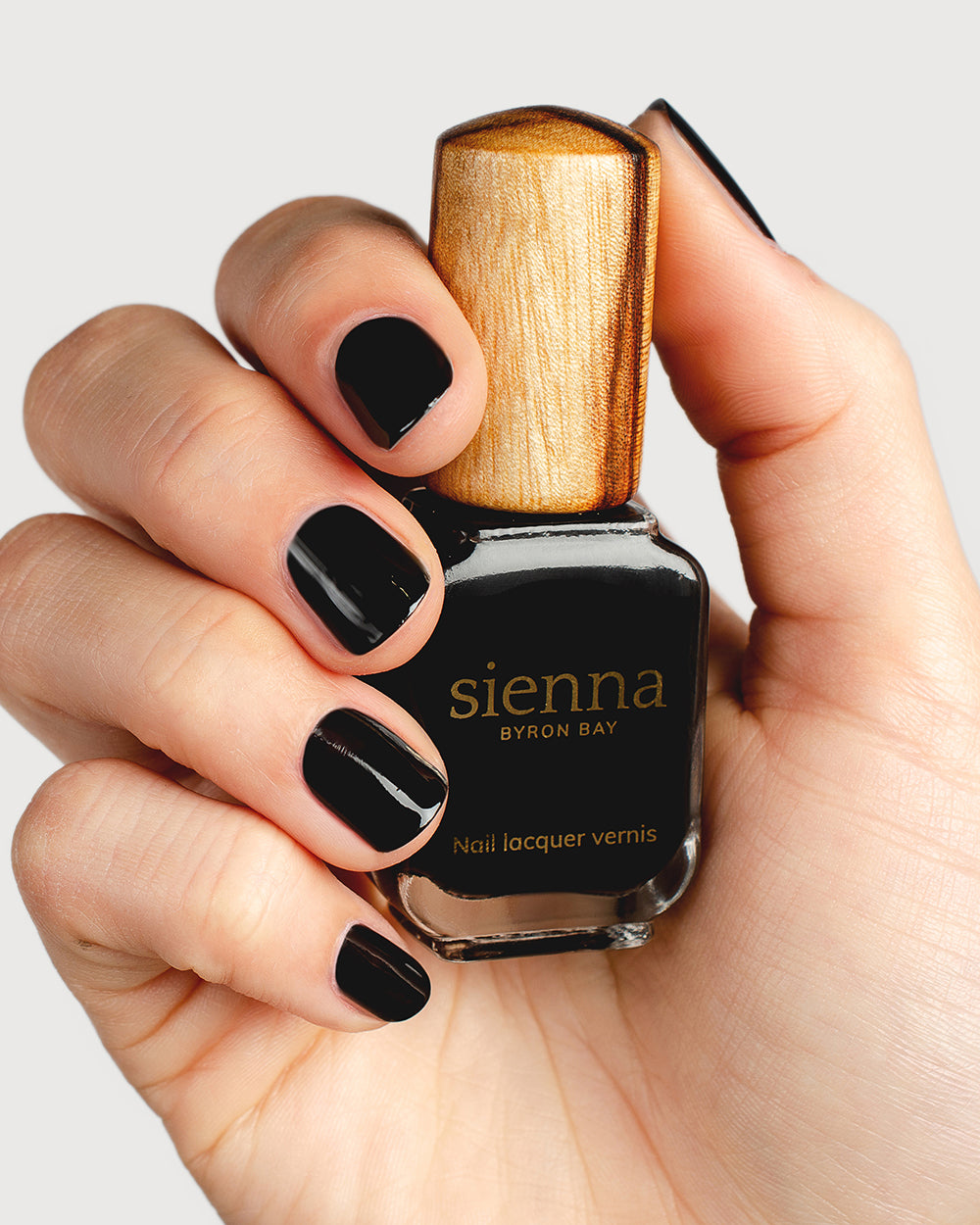 fair skin tone wearing black nail polish holding a sienna byron bay bottle