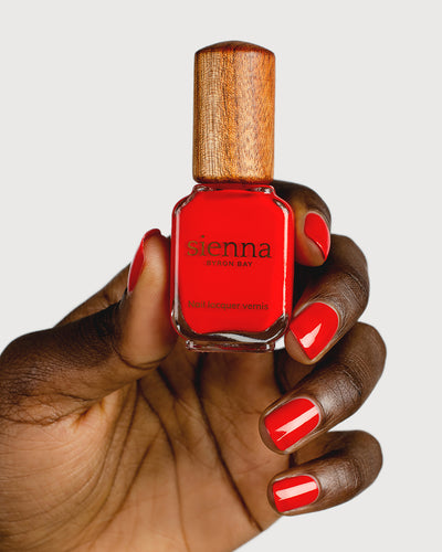 bright red nail polish hand swatch on dark skin tone holding sienna bottle