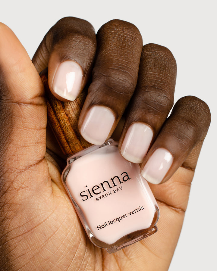 light rosewater pink sheer nail polish hand swatch on dark skin tone holding sienna bottle