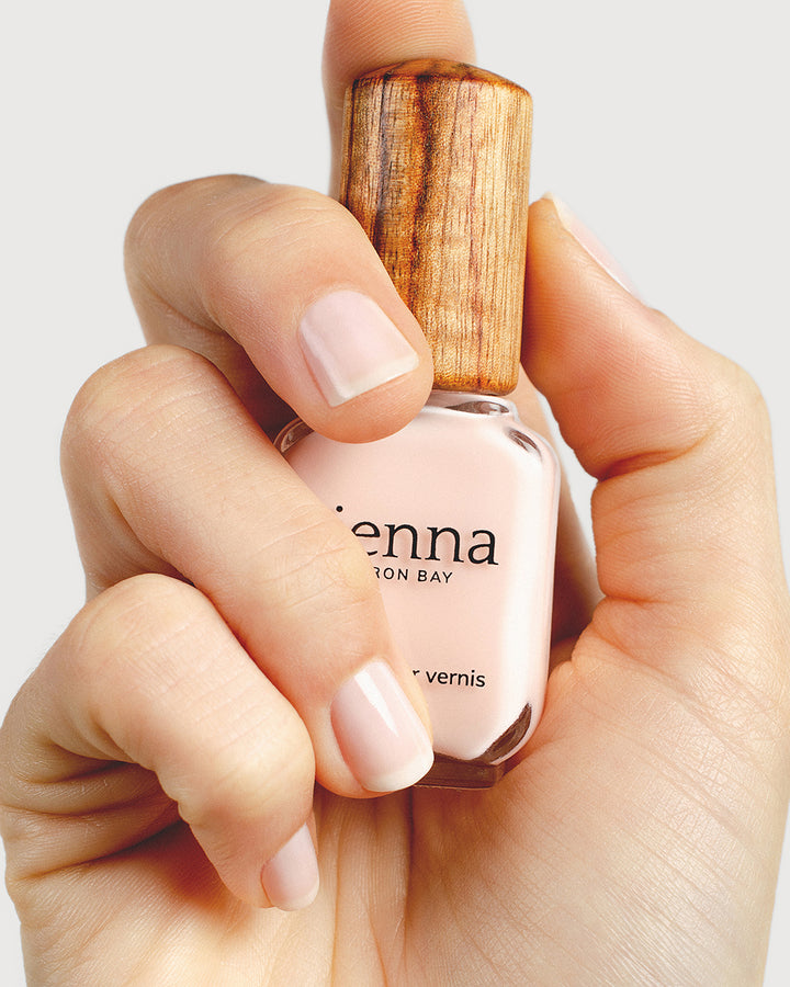 light rosewater pink sheer nail polish hand swatch on fair skin tone holding sienna bottle close up