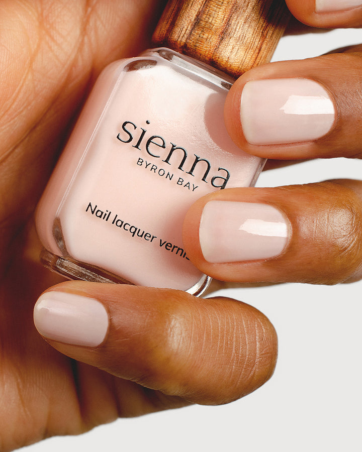 light rosewater pink sheer nail polish hand swatch on medium skin tone holding sienna bottle close up
