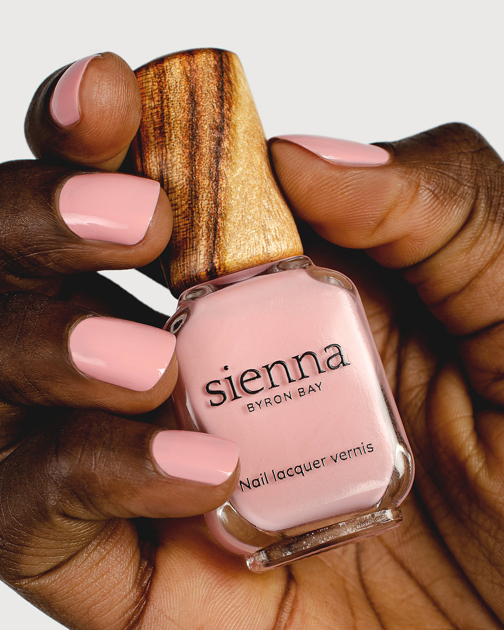 Cherry blossom pink nail polish hand swatch on dark skin tone holding sienna bottle close-up