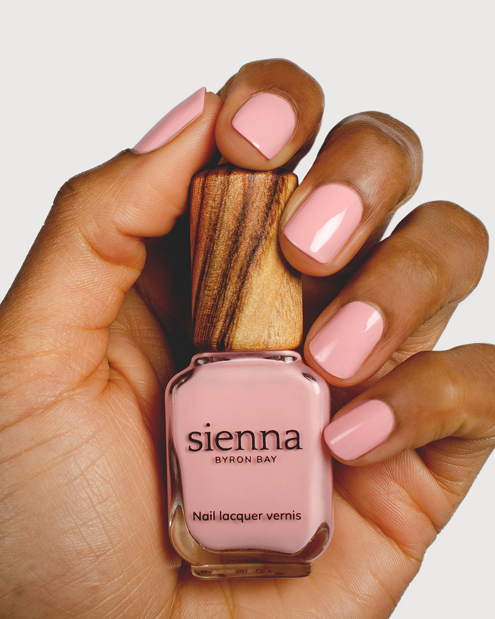 Cherry blossom pink nail polish hand swatch on medium skin tone holding sienna bottle close-up