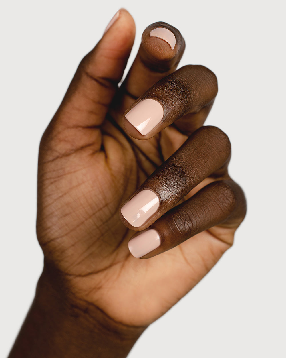 Soft neutral-pink nail polish hand swatch on dark skin tone