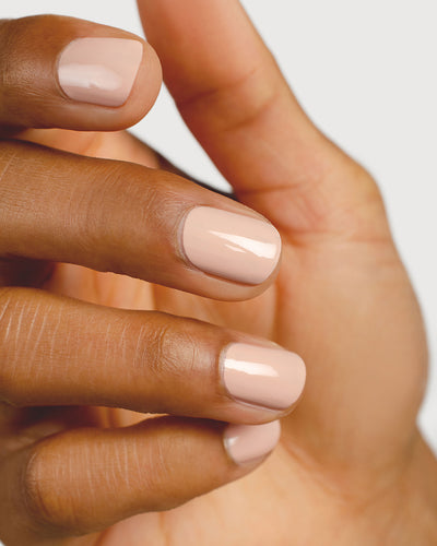 Soft neutral-pink nail polish hand swatch on medium skin tone close-up