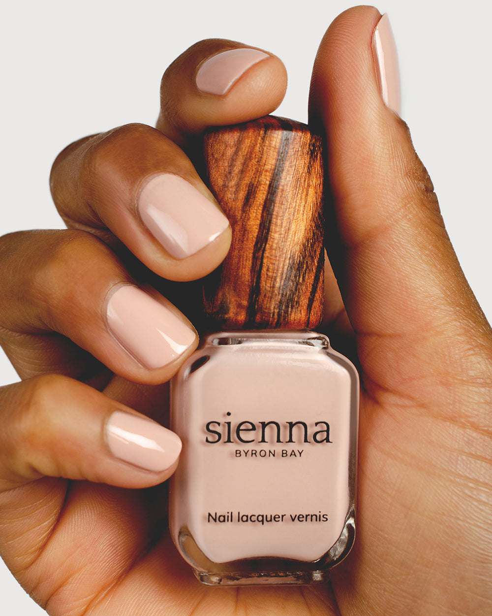 soft neutral-pink nail polish hand swatch on medium skin tone holding sienna bottle up close