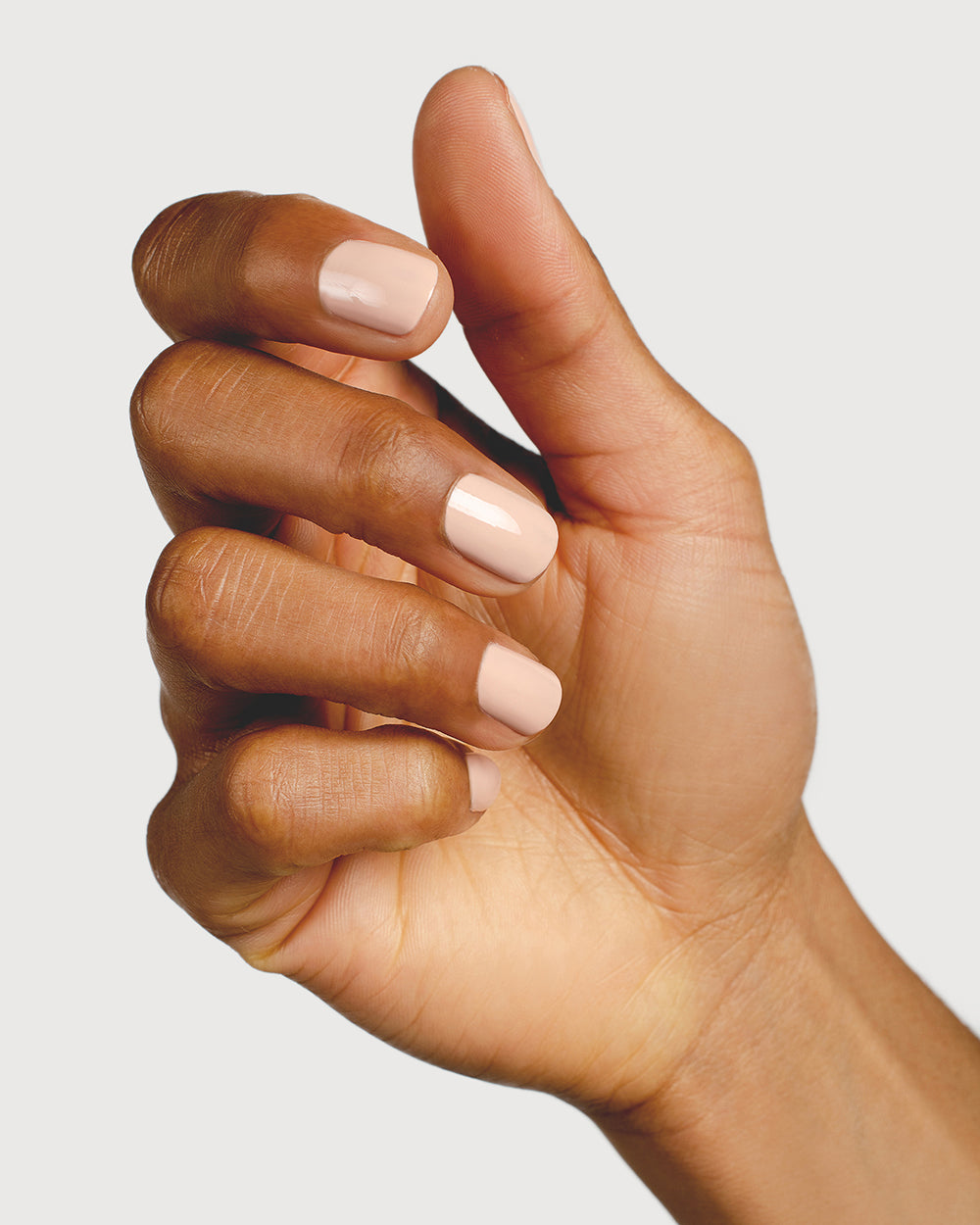 Soft neutral-pink nail polish hand swatch on medium skin tone