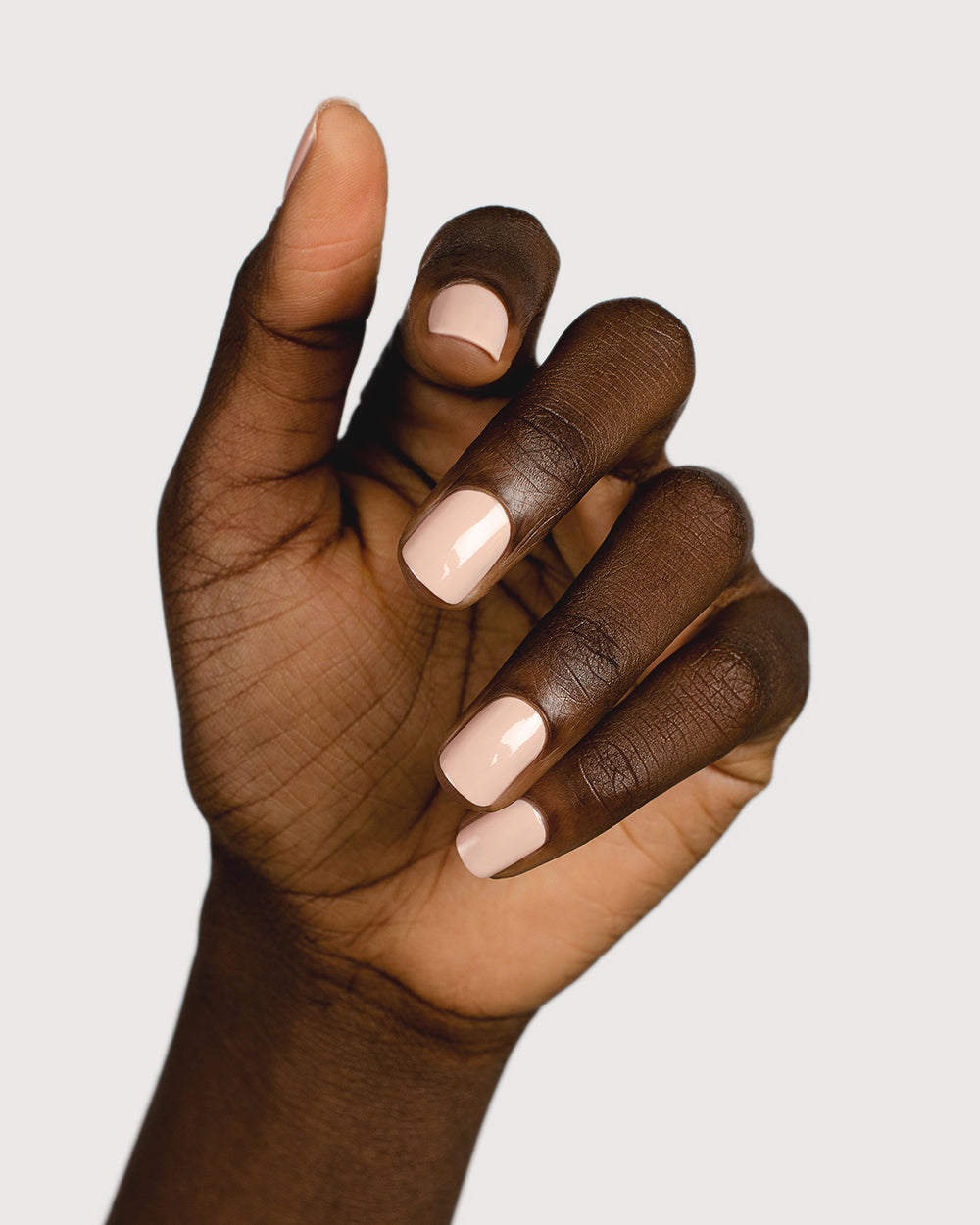 Soft neutral-pink nail polish hand swatch on dark skin tone