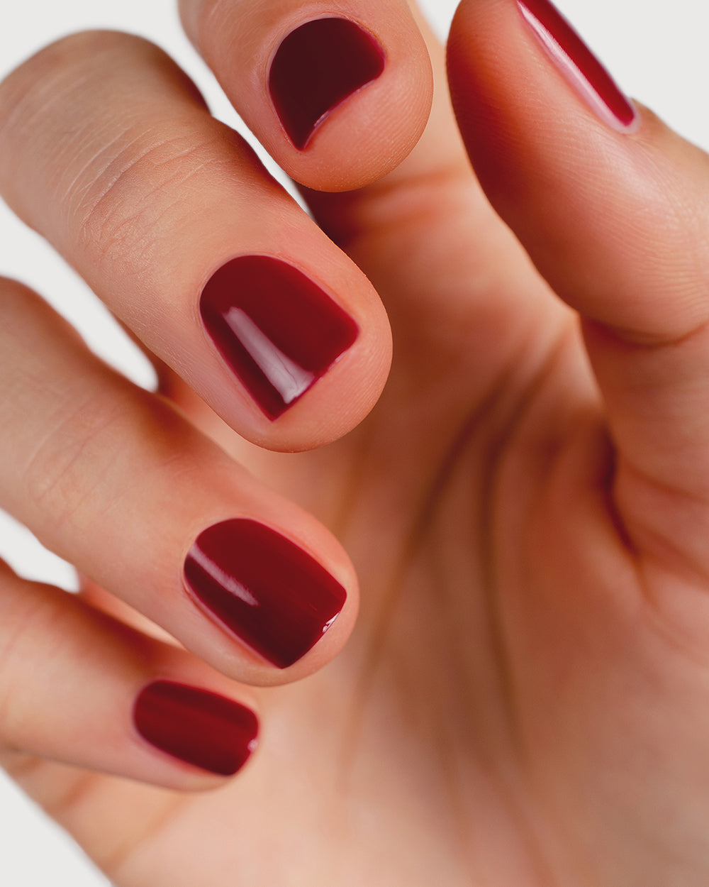Plum red nail polish hand swatch on fair skin tone up-close