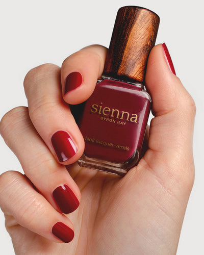 Plum red nail polish hand swatch on fair skin tone holding sienna bottle