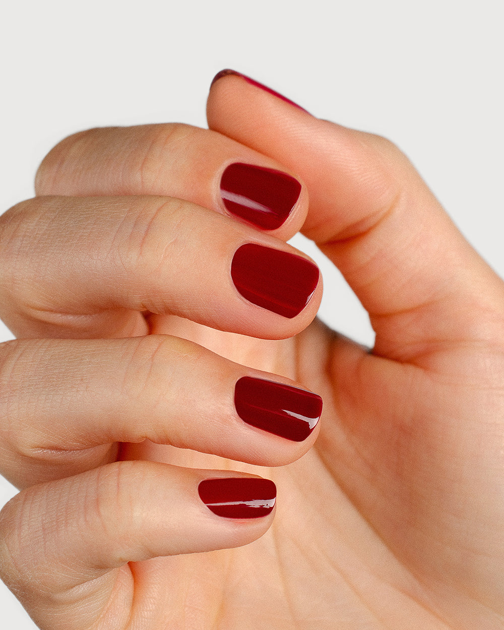 Plum red nail polish hand swatch on fair skin tone up-close