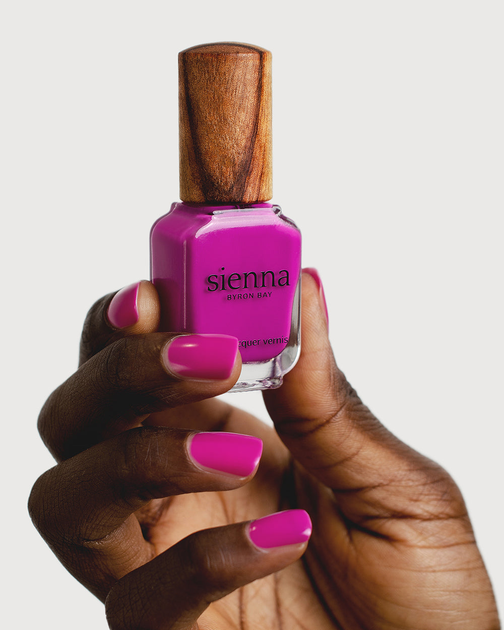Bright magenta nail polish hand swatch on dark skin tone holding sienna bottle 
