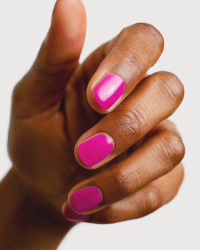 Bright magenta nail polish hand swatch on medium skin tone close-up
