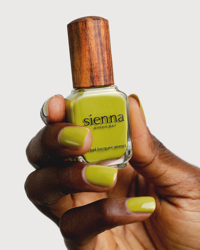 Avocado green nail polish hand swatch on dark skin tone holding sienna bottle close-up
