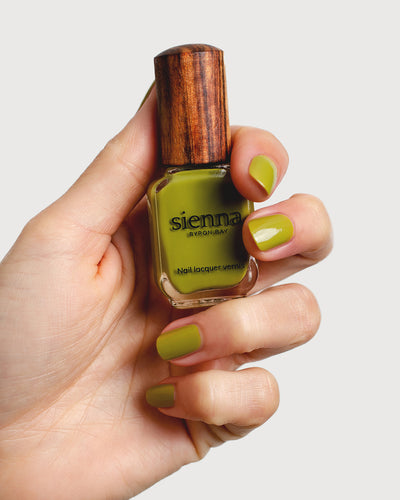 Avocado green nail polish hand swatch on fair skin tone holding sienna bottle