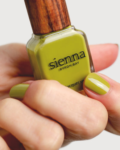 Avocado green nail polish hand swatch on fair skin tone holding sienna bottle close-up