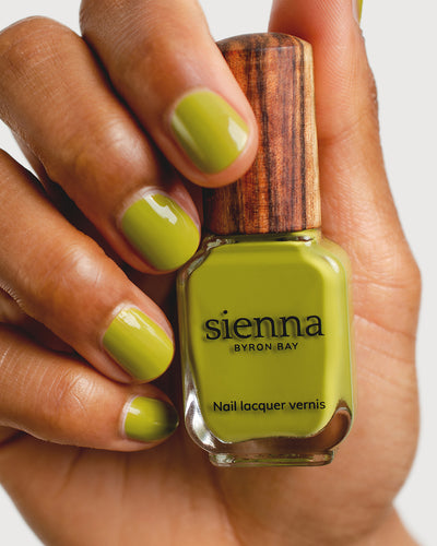 Avocado green nail polish hand swatch on medium skin tone holding sienna bottle close-up