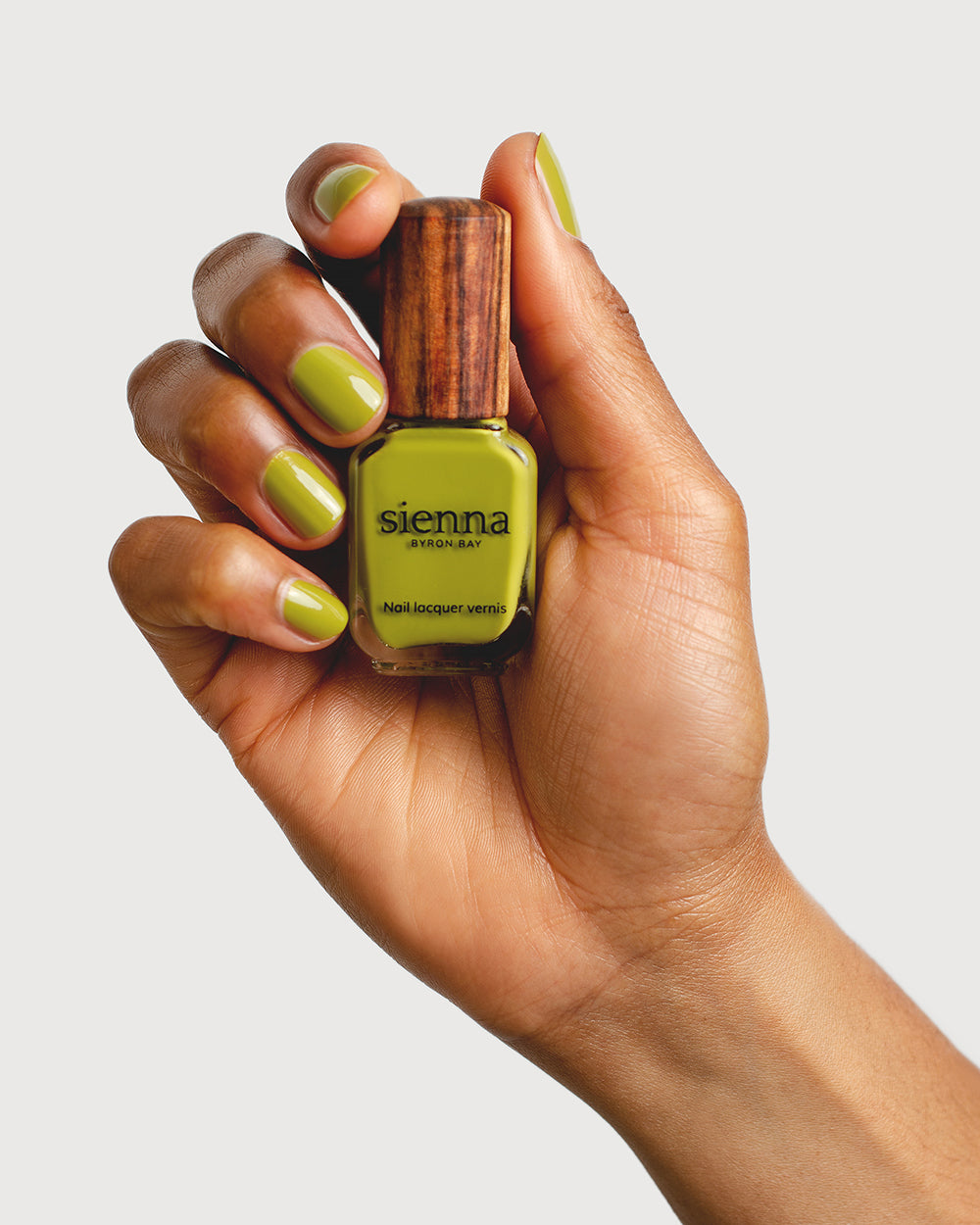 Avocado green nail polish hand swatch on medium skin tone holding sienna bottle