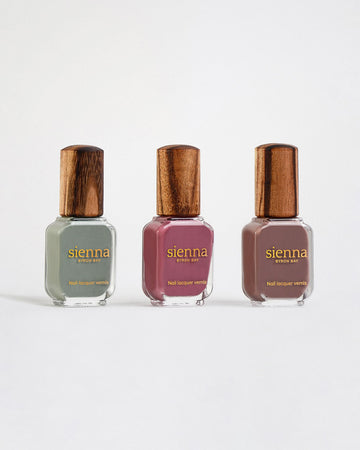 3 Sienna Nail polish bottles with gold logo Soundscape sage green, Heartscape raspberry sorbet and Grounded mylk chocolate crème Sienna nail polish bottles with timber lids on a light grey-cream background.