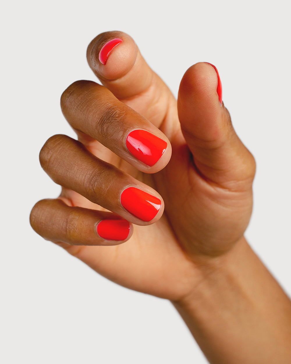 Warm strawberry red nail polish hand swatch on medium skin tone