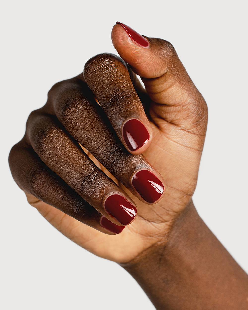 Organic mid-tone red nail polish hand swatch on dark skin tone