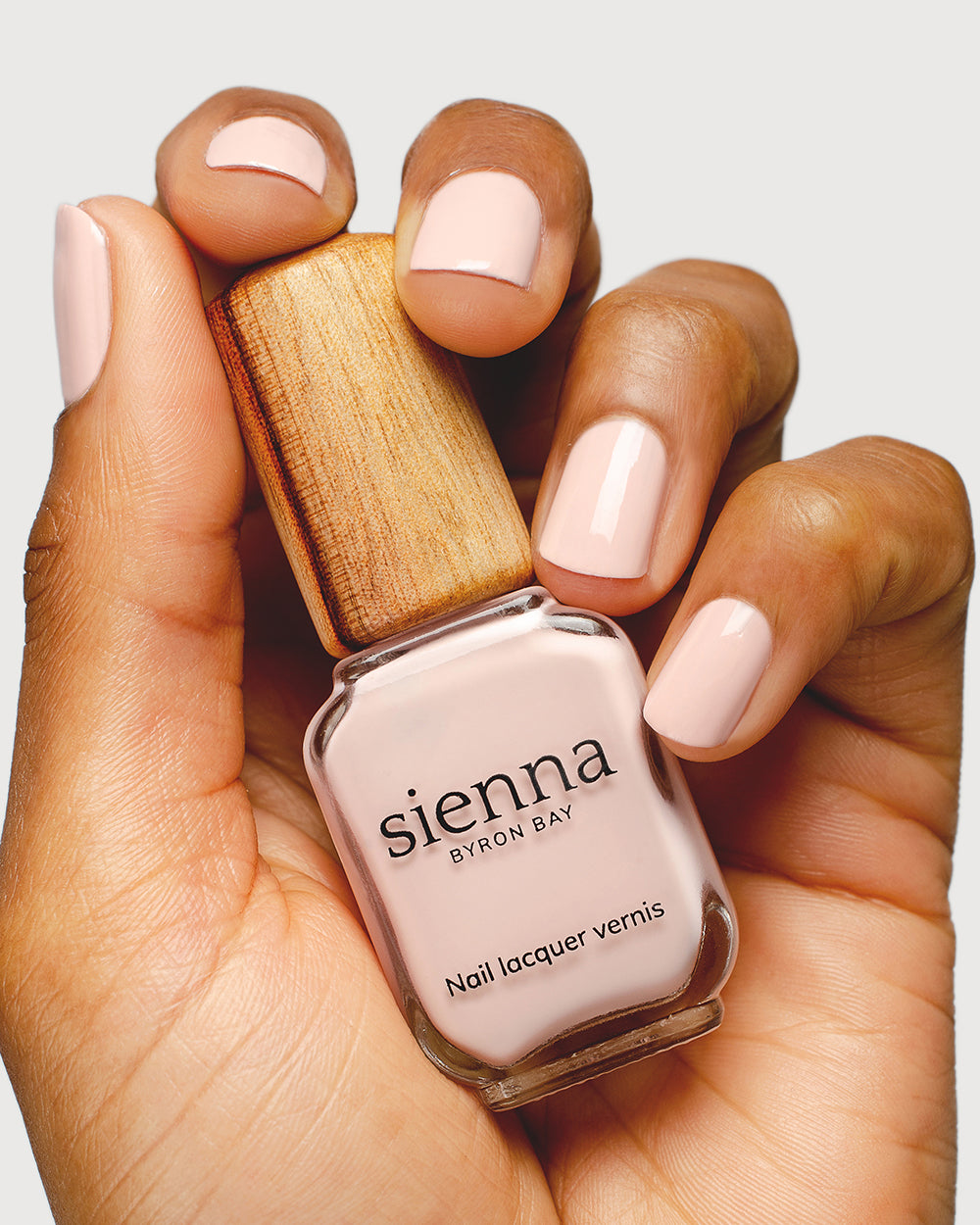Light champagne pink nail polish hand swatch on medium skin tone up-close holding sienna bottle