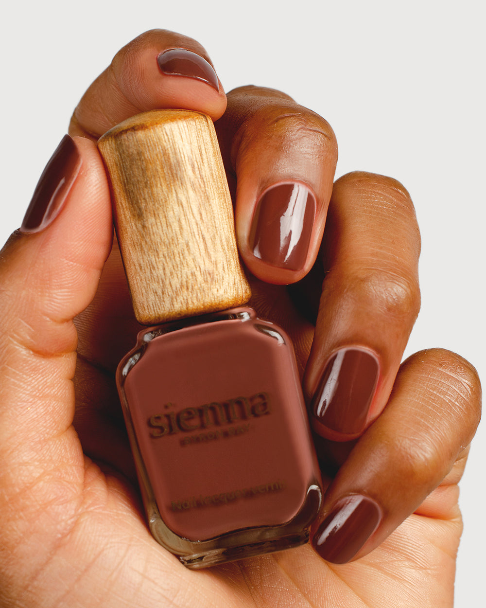brown nail polish hand swatch on medium skin tone holding a sienna bottle