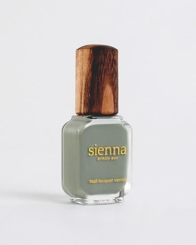 Soundscape sage green crème Sienna nail polish bottles with with gold logo and timber lids on a light grey-cream background.
